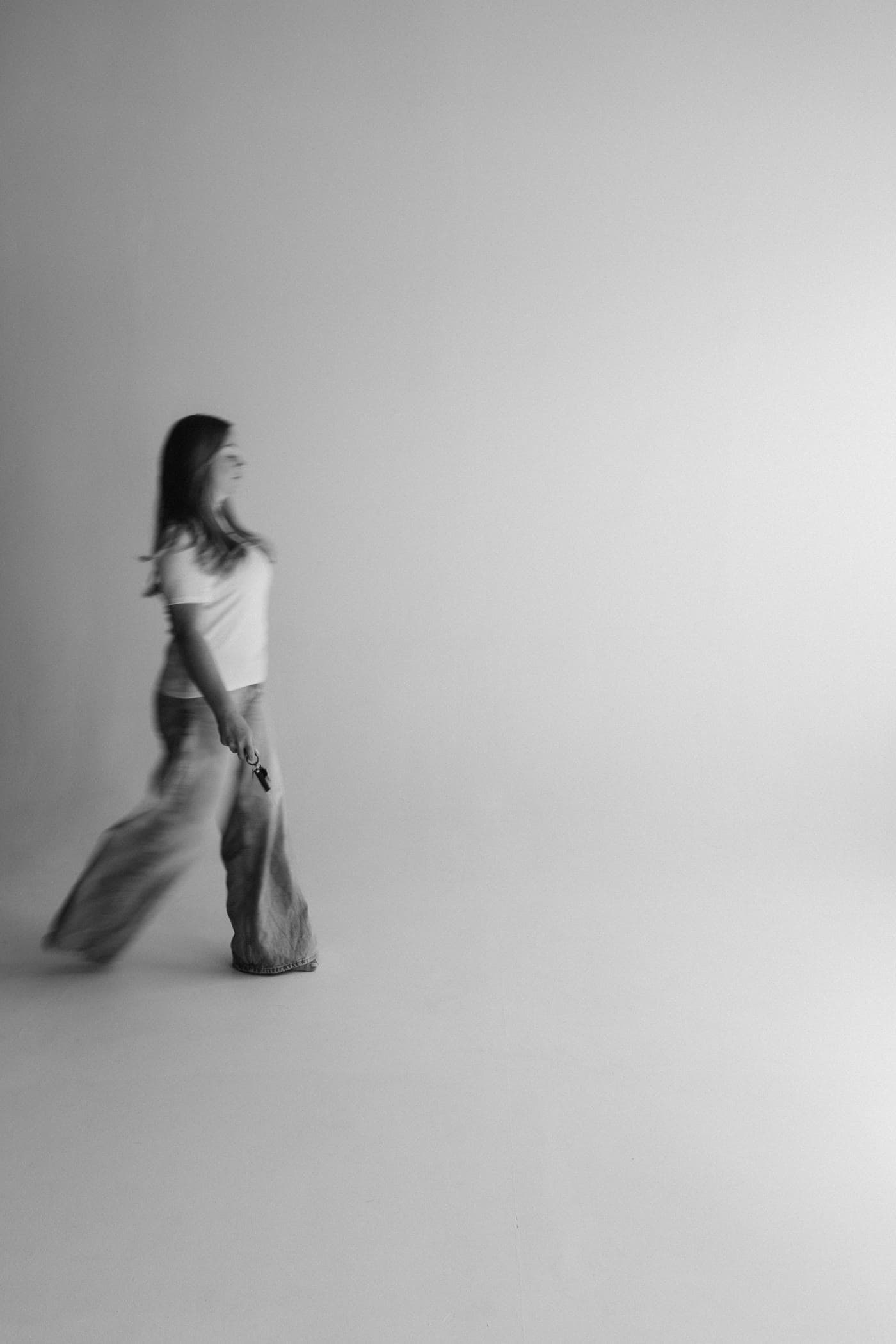 A woman walking across a pale, empty studio, black and white.